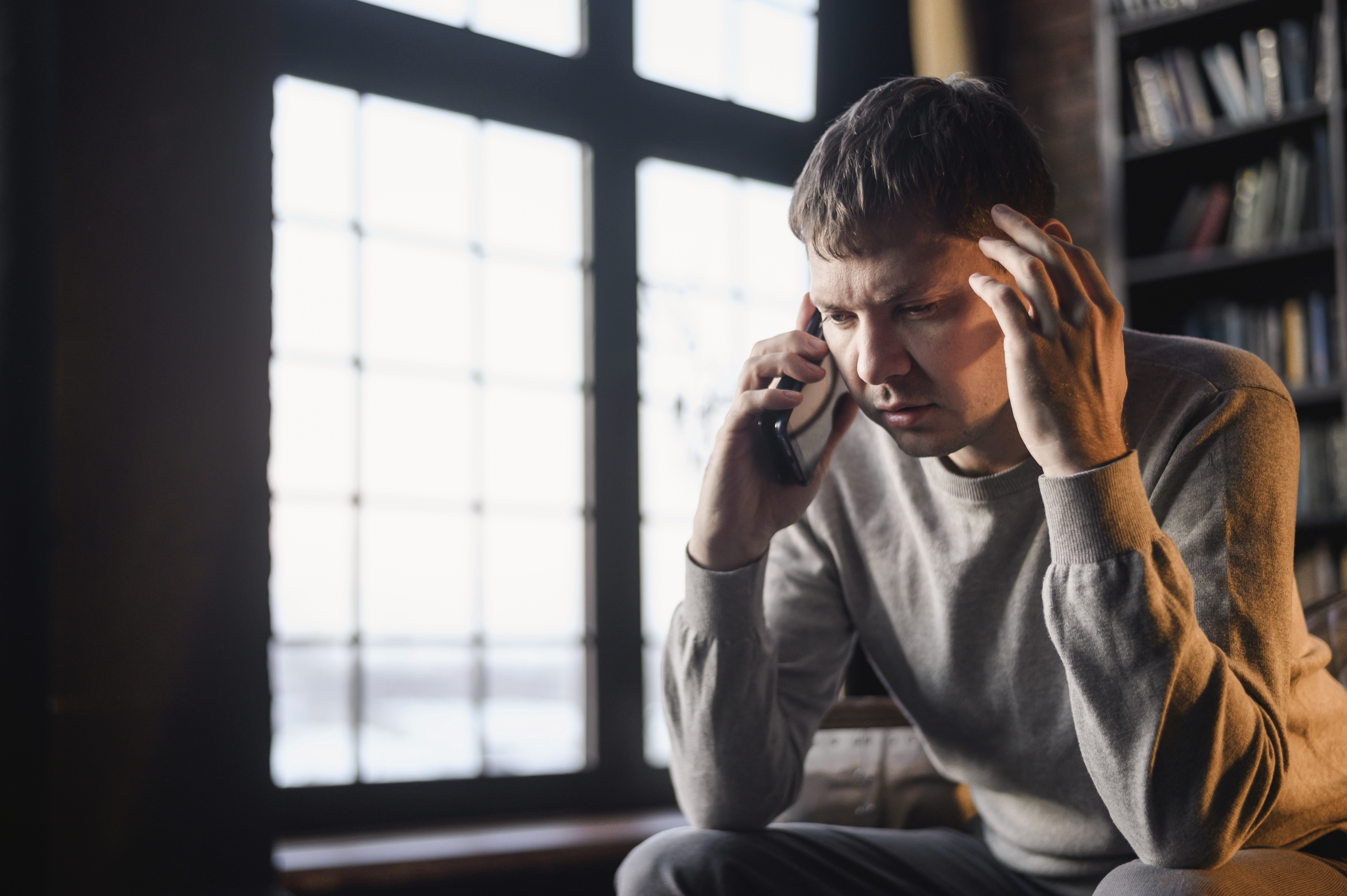 A young adult male with a worried facial expression talking on the phone